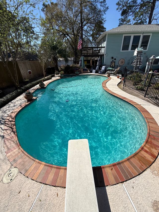 Kidney-shaped pool with clear turquoise water, red brick coping and a white diving board