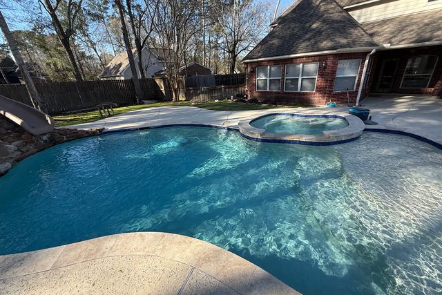 Freeform pool with an attached round spa and clear blue water, a brick house behind it