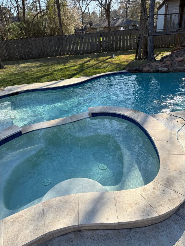 Round spa with clear water next to a freeform pool, with lawn and tall trees behind