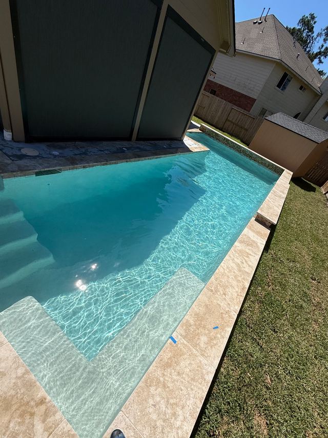 Long rectangular pool with a shallow sun ledge, travertine coping and green lawn alongside
