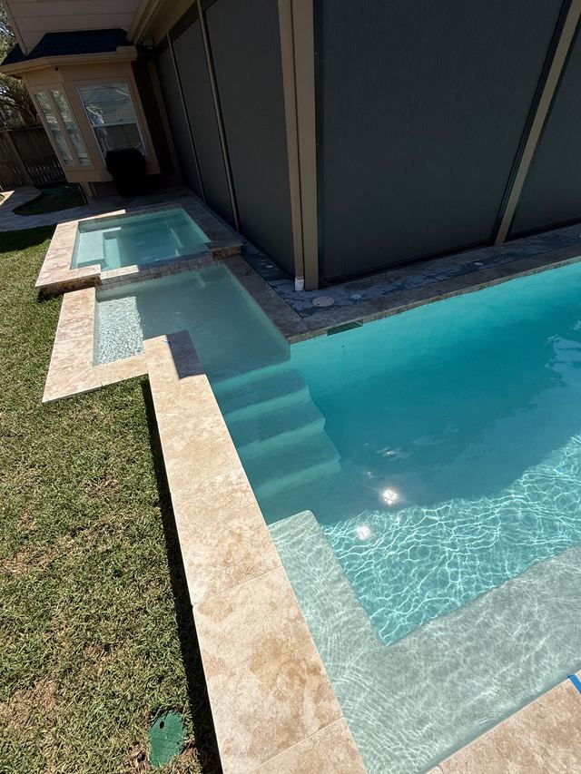 Raised spa spilling toward a pool with wide entry steps and travertine edging on a lawn