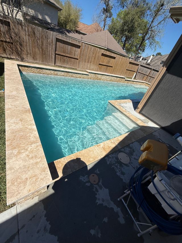Rectangular pool with clear water and entry steps, a wooden fence behind it